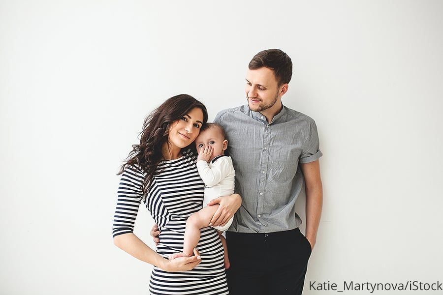 Eltern mit Baby beim Familienfoto vor weißer Wand.